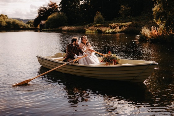 Bride and groom smile at each other in rowboat on Cardney Estate